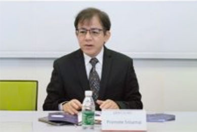 A speaker in a suit and tie seated at a table with a name placard, presenting on labour law amendments.
